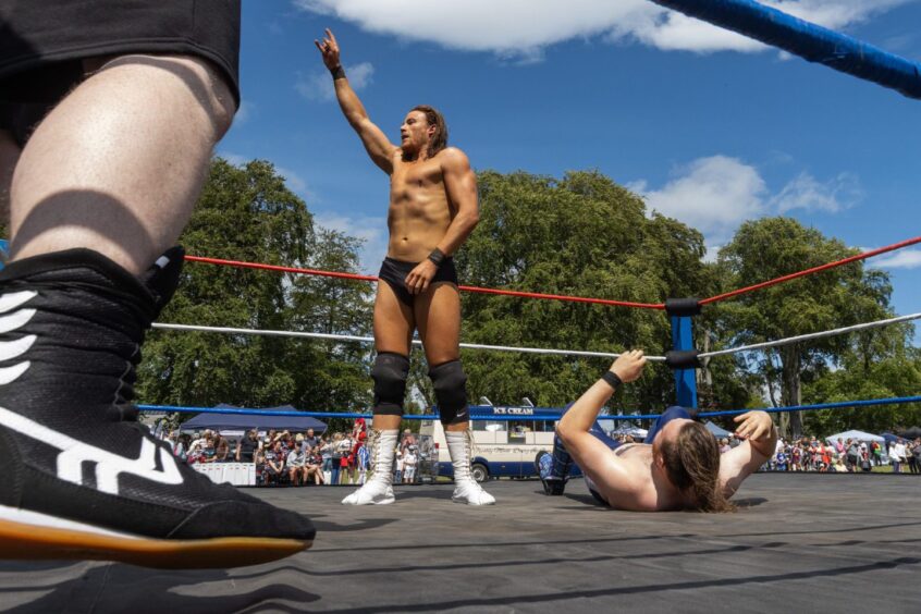 SWE wrestler raises his hand in victory while another competitor lies on the mat during a live wrestling event at Carnoustie gala day 2025.