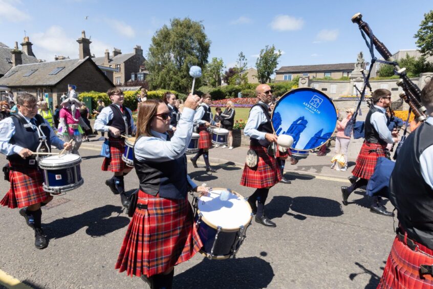 Members of the Arbroath Pipe Band perform in tartan kilts during the Carnoustie gala day parade, playing drums and bagpipes for the cheering audience.