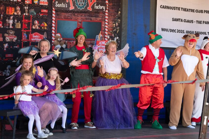 Group dressed in festive costumes including elves, fairies and a reindeer wave from a decorated float promoting Carnoustie Theatre Club’s 2025 Christmas panto.