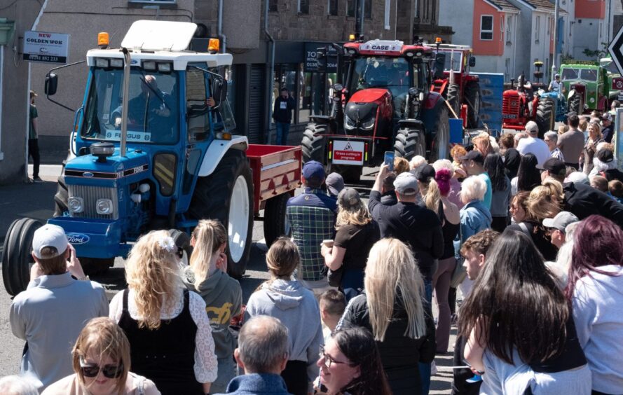A mix of vintage and modern tractors drive past crowds in Carnoustie during the 2025 gala day, including blue Ford and red Case IH models.