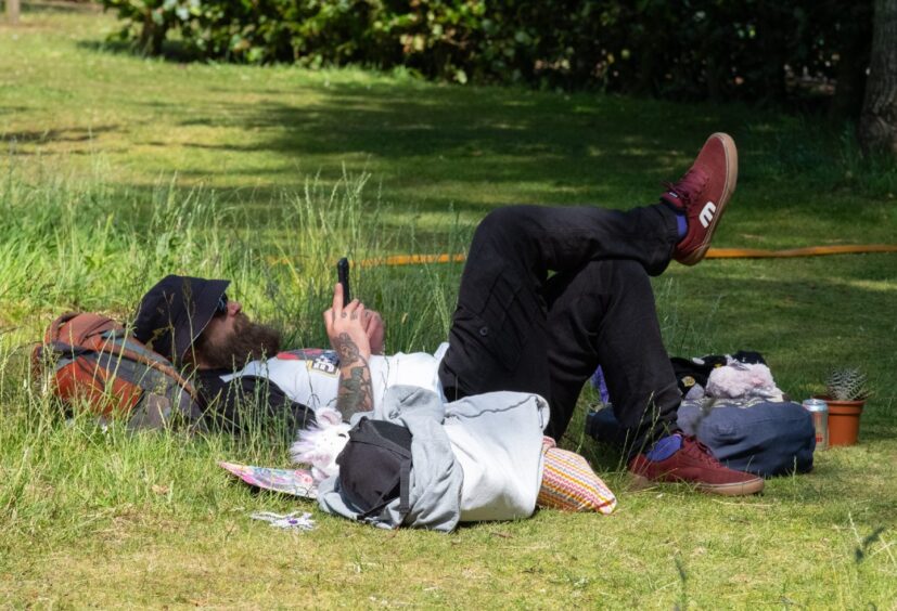 Man lies in the grass looking at his phone during a quiet moment at Carnoustie gala 2025.