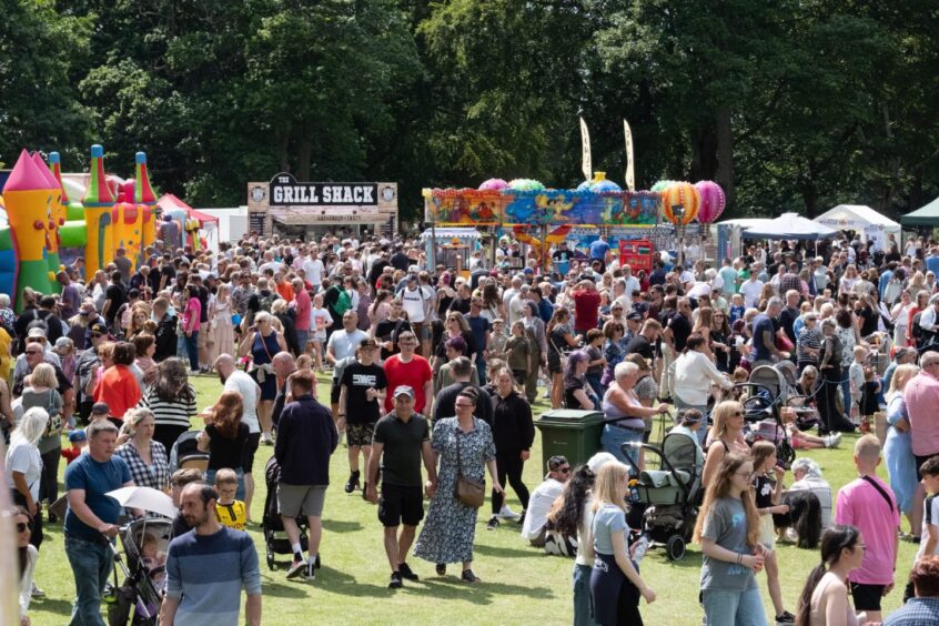 Large crowd at Carnoustie gala day 2025 with bouncy castles, food stalls and colourful fairground rides set up in the background on the green.