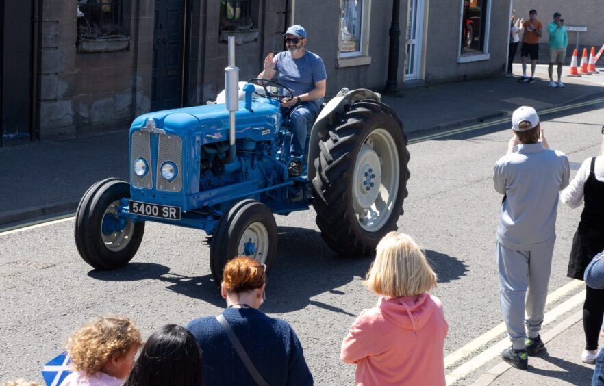 Driver waves from a classic blue Fordson tractor as it passes through Carnoustie town centre during the 2025 gala day parade.