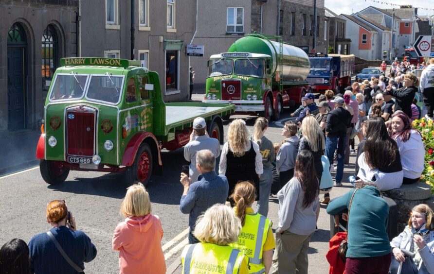 Classic green and red Harry Lawson lorries drive past cheering spectators during the 2025 Carnoustie gala day float parade.