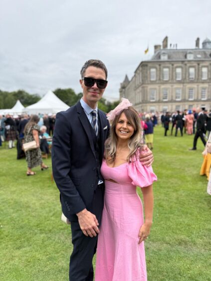 Cameron and Debra Grassick, smiling with palace and garden party behind