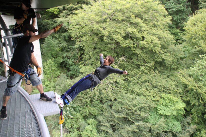 Person bungeeing off bridge platform with treetops below