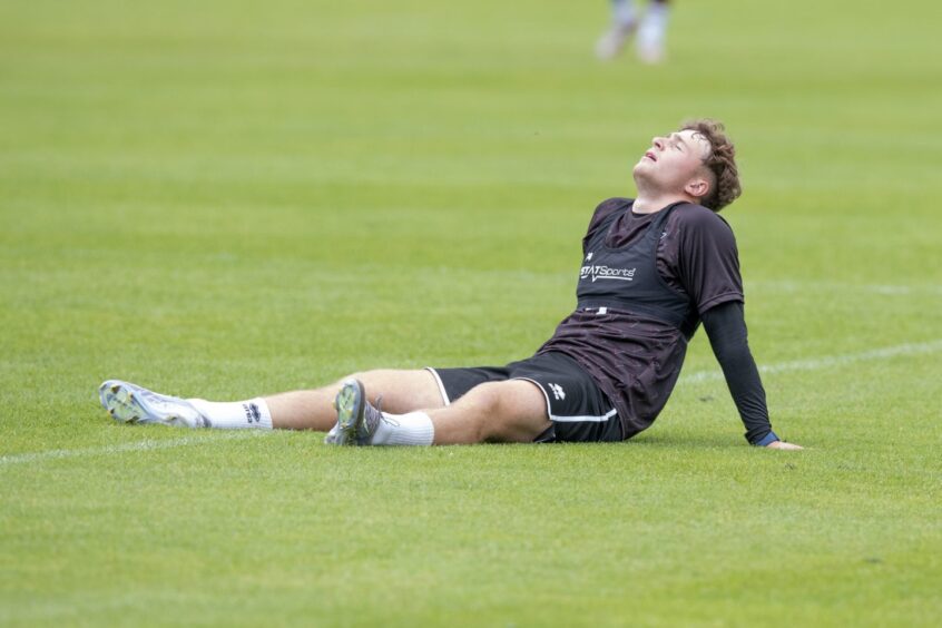 An exhausted-looking Taylor Sutherland sits on the grass.