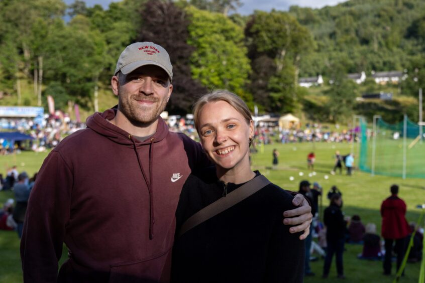 Young couple arm in arm with highland games field behind them