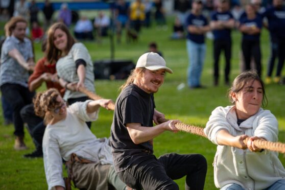 People doing tug of war, one in a cap smiling while the one behind falls over