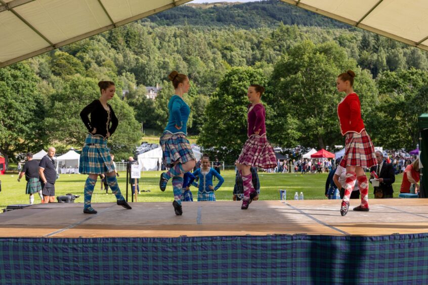girls in kilts doing Scottish Highland dancing with trees and mountains behind