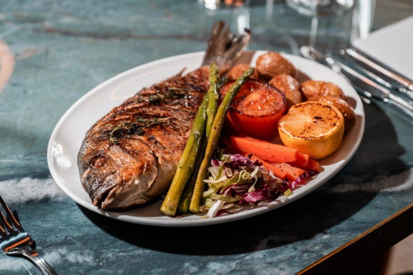 A plate filled with a whole grilled sea bream.