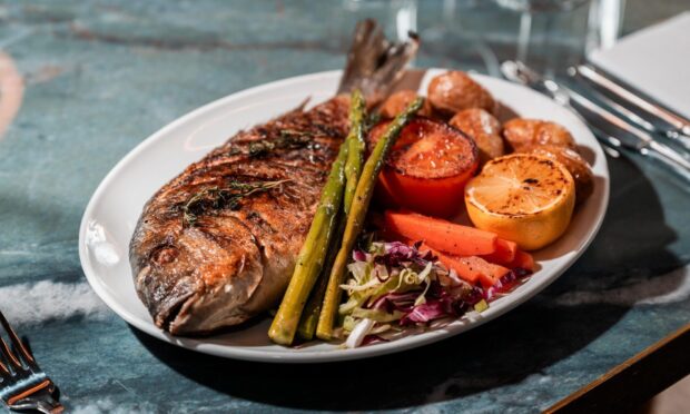 A plate filled with a whole grilled sea bream.