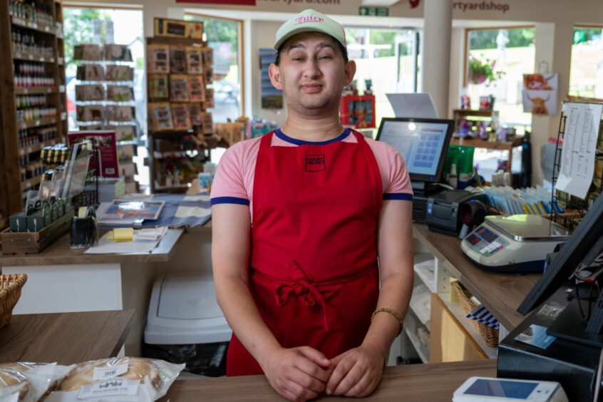 Valentino Murdoch in red apron behind counter in Taymouth shop