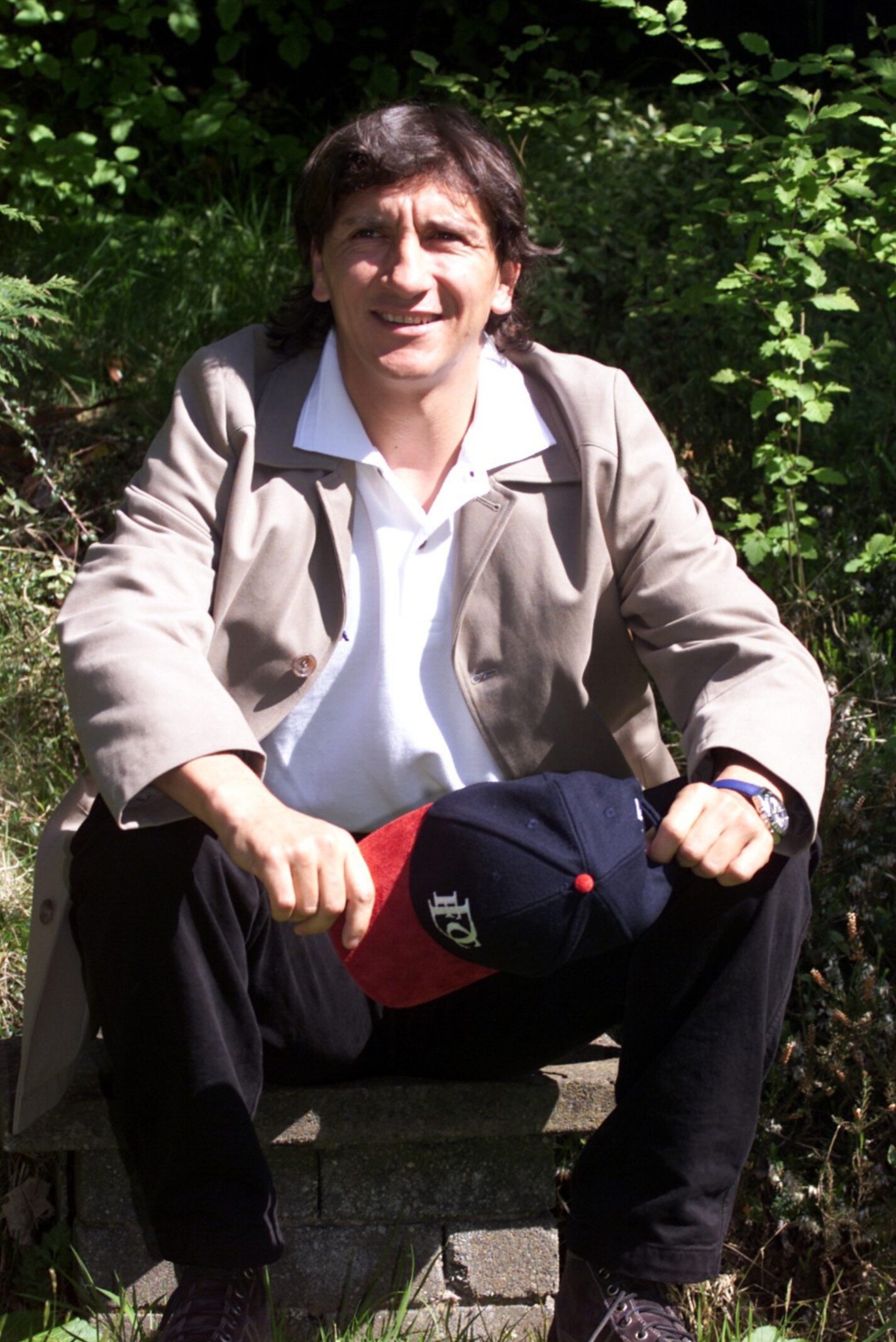 A smiling Ivano Bonetti sitting down in the sunshine and holding a Dundee FC cap