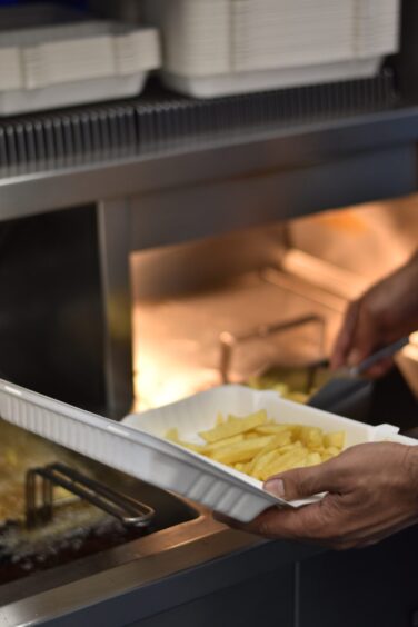 Cooked chips being added into a tray.