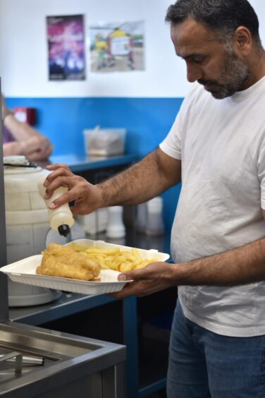 Kamran Ishaq pouring vinegar on the fish and chips.