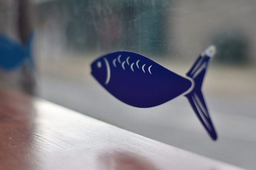 A decal showing a fish on the window of The Plaice To Be in Pitlochry.