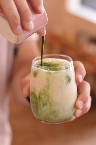 Matcha being poured into a glass of iced oat milk.