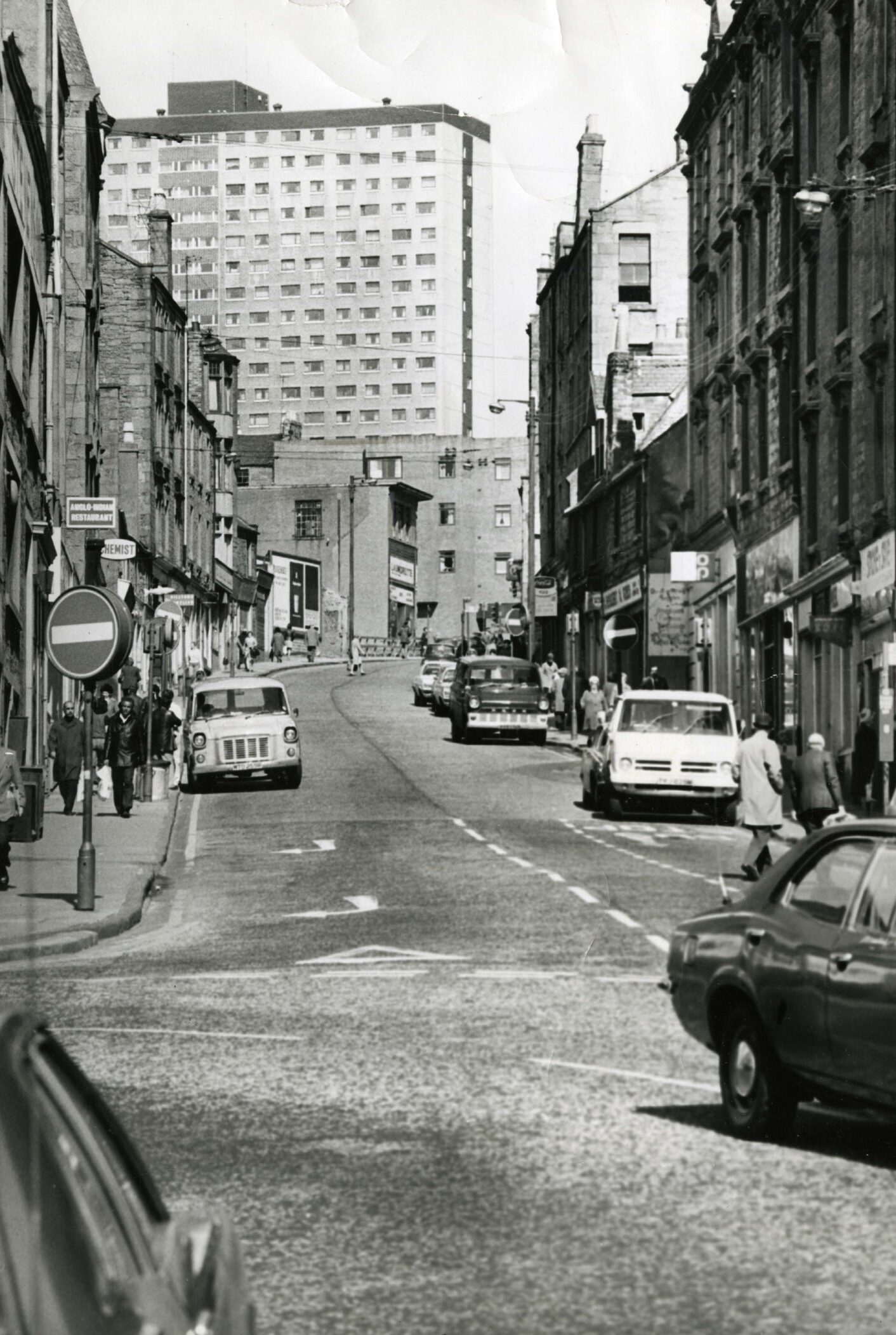 a shot looking uphill that show pedestrians, Hilltown shops and high rises.