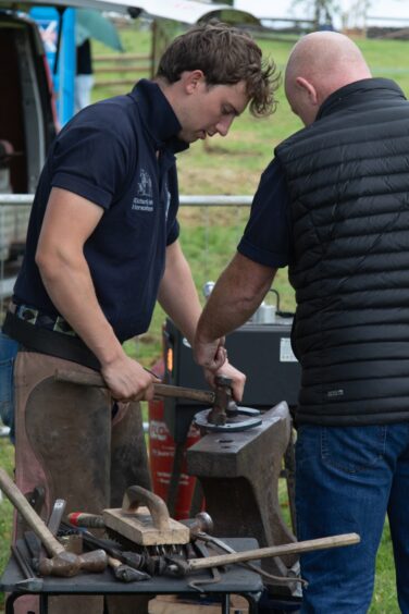 Farrier in navy shirt and leather apron hammers metal on an anvil at Doune and Dunblane Show 2025.