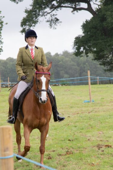 Female equestrian in a check jacket and red tie rides chestnut horse with plaited mane at Doune and Dunblane Show 2025.