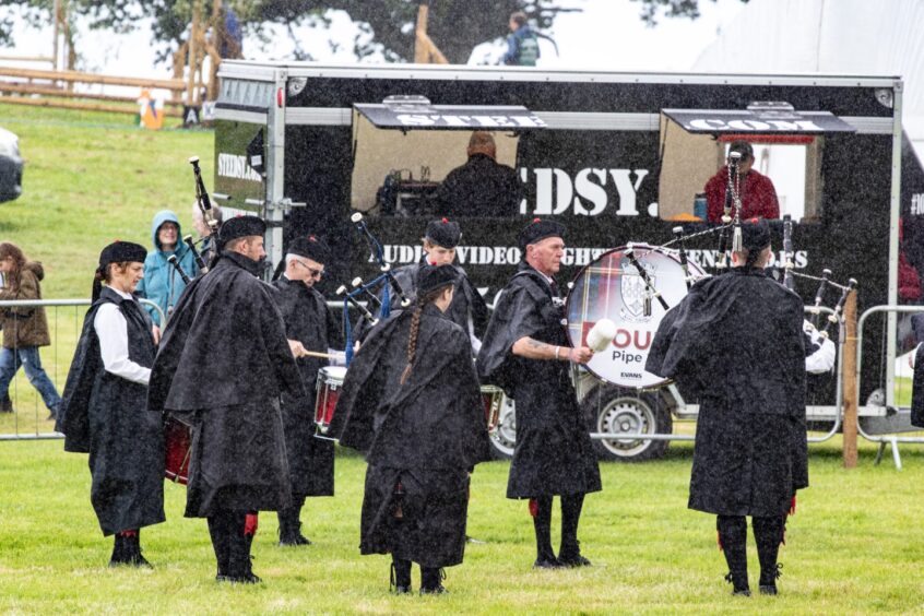 Doune Pipe Band play in wet weather wearing black capes at Doune and Dunblane Show 2025.