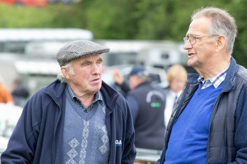 Two older men chatting outdoors at Doune and Dunblane Show 2025, one wearing a flat cap and the other in a blue jumper.