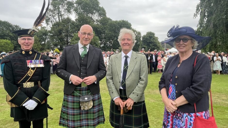 Four people, including First Minister John Swinney in kilt and man in uniform of Royal Company of Archers at garden party