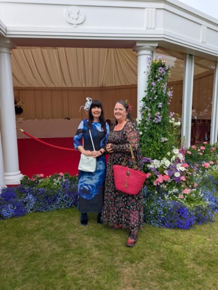 Marie Morris with Helen Quinn in front of tent with floral displays.