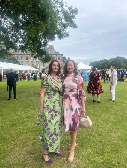 Heather Anderson and Nichola Ward in dresses in front of palace and garden party