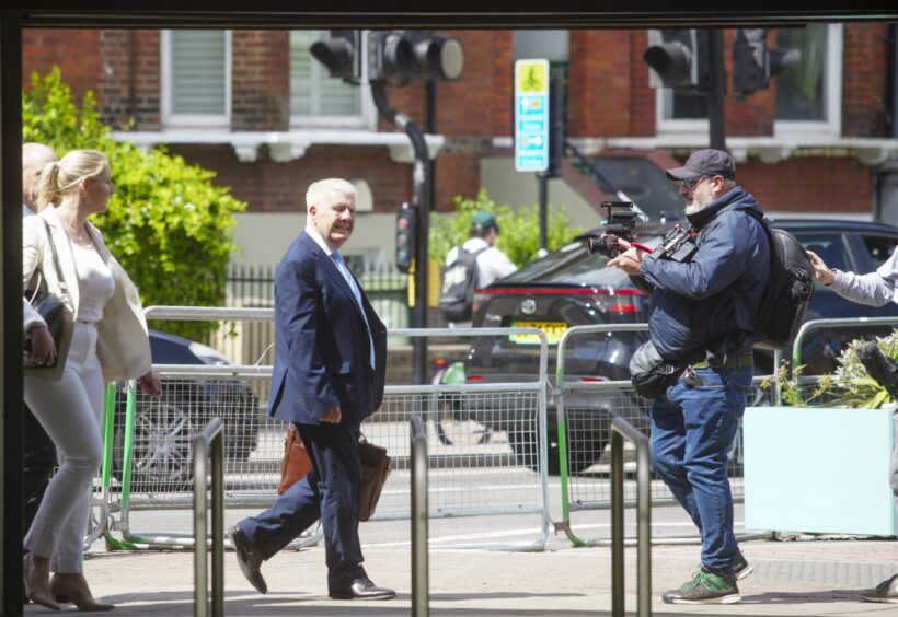 Sir Wyn Williams in suit carrying briefcase as he walks towards camera crews in London street