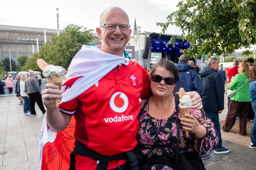 A man in a Wales rugby top and his partner enjoy an ice cream.