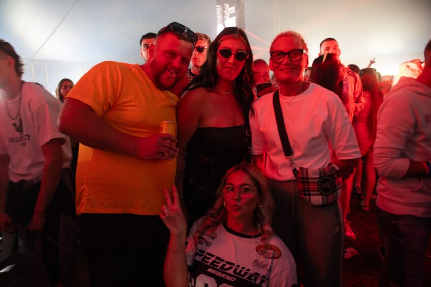 Four friends smiling and posing under red lighting in the packed tent at doof in the Park 2025, Dundee.