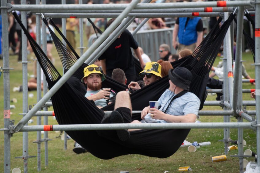 Group of men lounging in black hammocks under scaffold frames at doof in the Park 2025, Camperdown Park, Dundee.