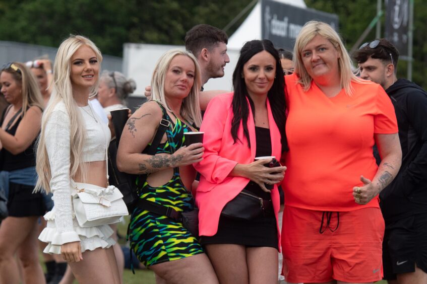 Four women dressed in vibrant festival outfits smiling and posing at doof in the Park 2025, Camperdown Park, Dundee.