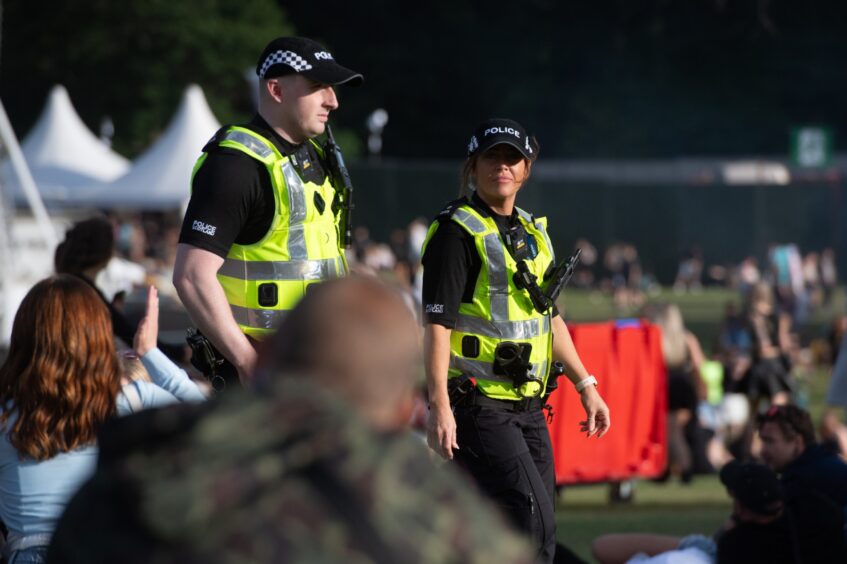 Two uniformed police officers on patrol among festival-goers at doof in the Park 2025, Camperdown Park, Dundee.