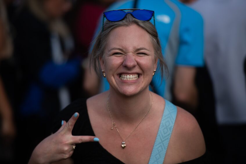 Woman grinning widely and flashing a peace sign at doof in the Park 2025, Camperdown Park, Dundee.