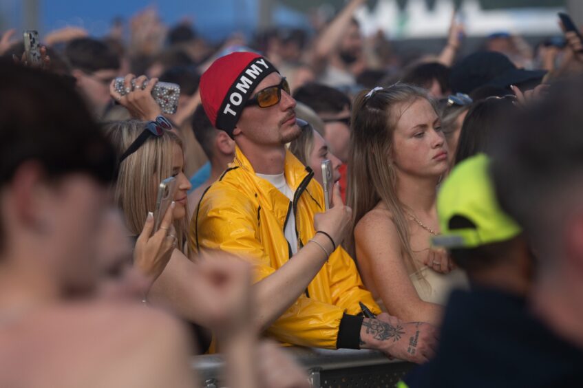 Festival-goers at the front barrier filming with phones and watching a performance at doof in the Park 2025, Camperdown Park, Dundee.