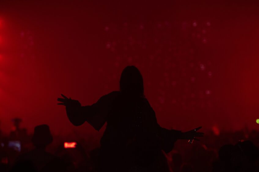 Silhouette of a person dancing on someone’s shoulders in red lighting during a night set at doof in the Park 2025, Camperdown Park, Dundee.