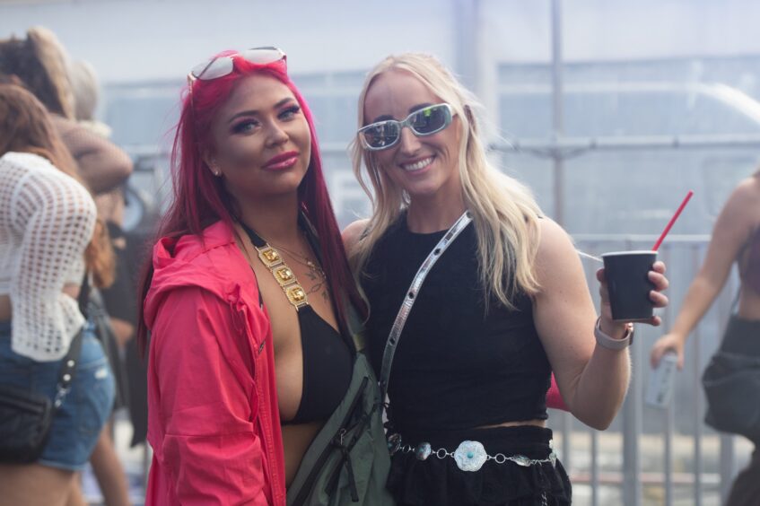 Two women posing and smiling in stylish festival outfits inside a tent at doof in the Park 2025, Camperdown Park, Dundee.