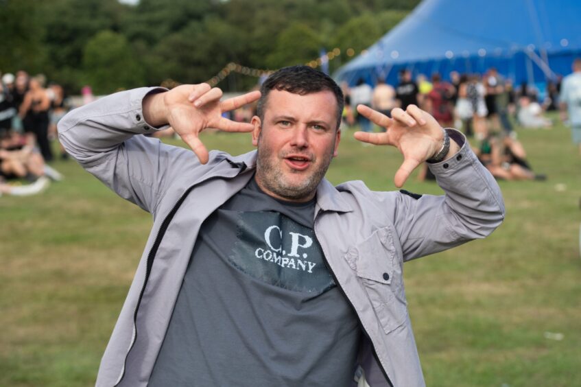 Man striking a playful pose with hands up near his face at doof in the Park 2025, Camperdown Park, Dundee.
