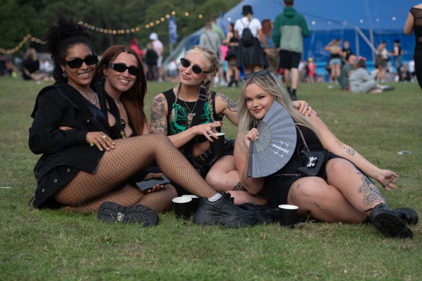 Four women sitting on the grass with drinks and a fan at doof in the Park 2025 at Camperdown Park, Dundee.