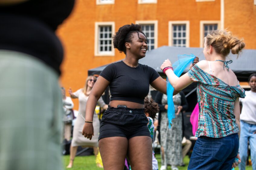 Two young women dancing with blue scarves in front of an orange building at the Afro-Caribbean Summer Festival in Pittencrieff Park.