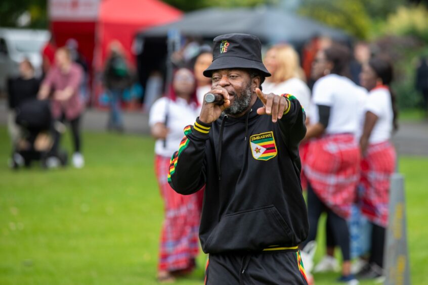 Daddy Slaggy performs in a Zimbabwe tracksuit, holding a microphone and pointing to the crowd at the Afro-Caribbean Summer Festival in Pittencrieff Park.