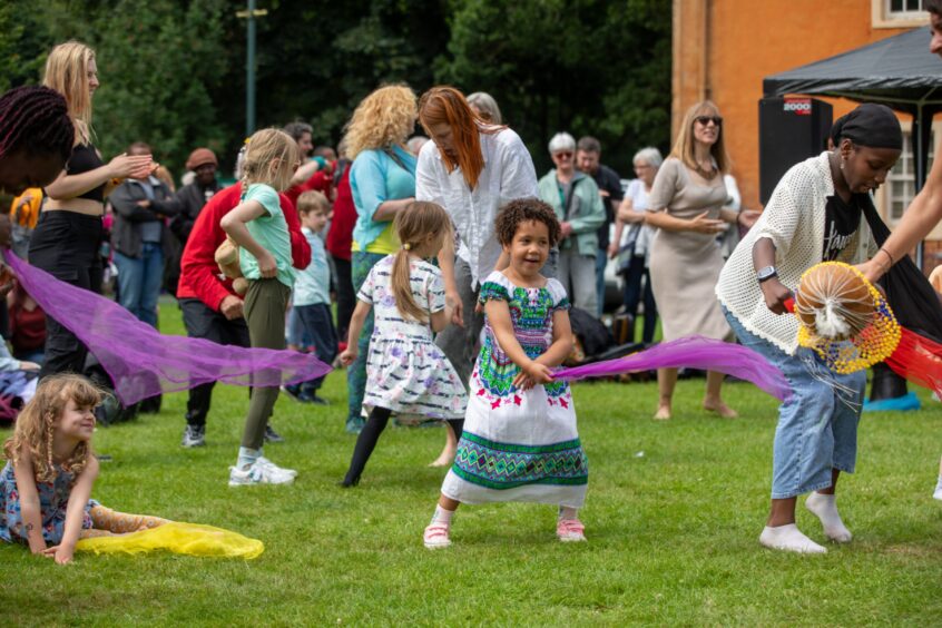 Children dance with purple and yellow scarves on the grass as part of a cultural activity at the Afro-Caribbean Summer Festival in Dunfermline.