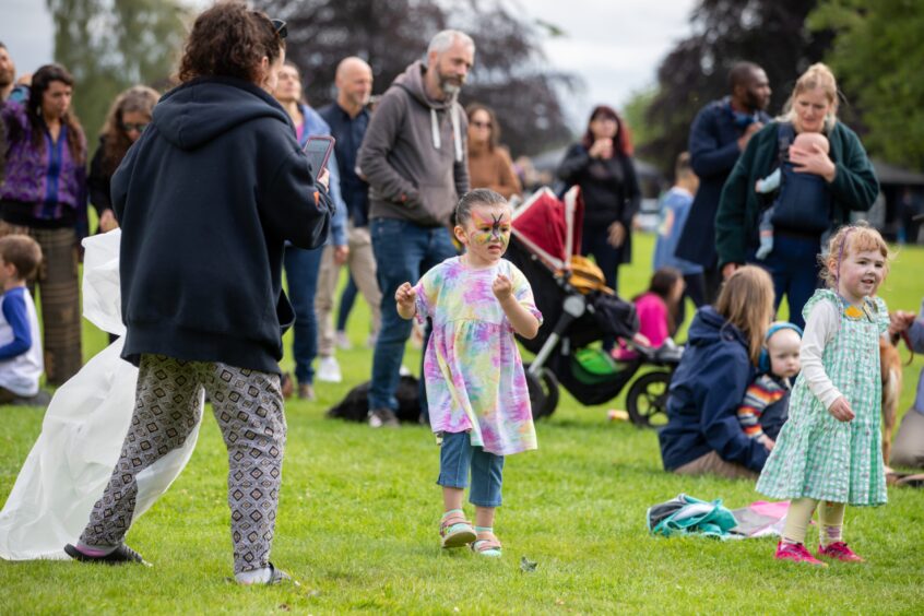 Children with face paint play on the grass surrounded by families and buggies at the Afro-Caribbean Summer Festival in Pittencrieff Park, Dunfermline.