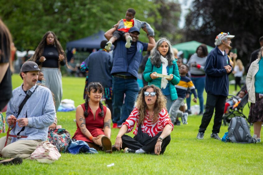 People of all ages sit and stand in a relaxed festival crowd at Pittencrieff Park during the Afro-Caribbean Summer Festival in Dunfermline.