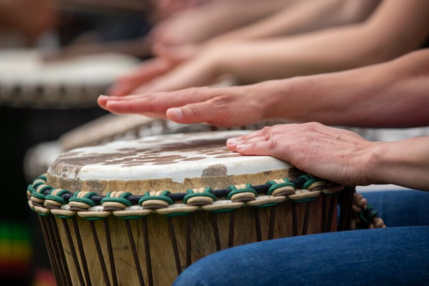 Close-up of hands playing a traditional djembe drum at the Afro-Caribbean Summer Festival in Dunfermline, showcasing cultural music activities.