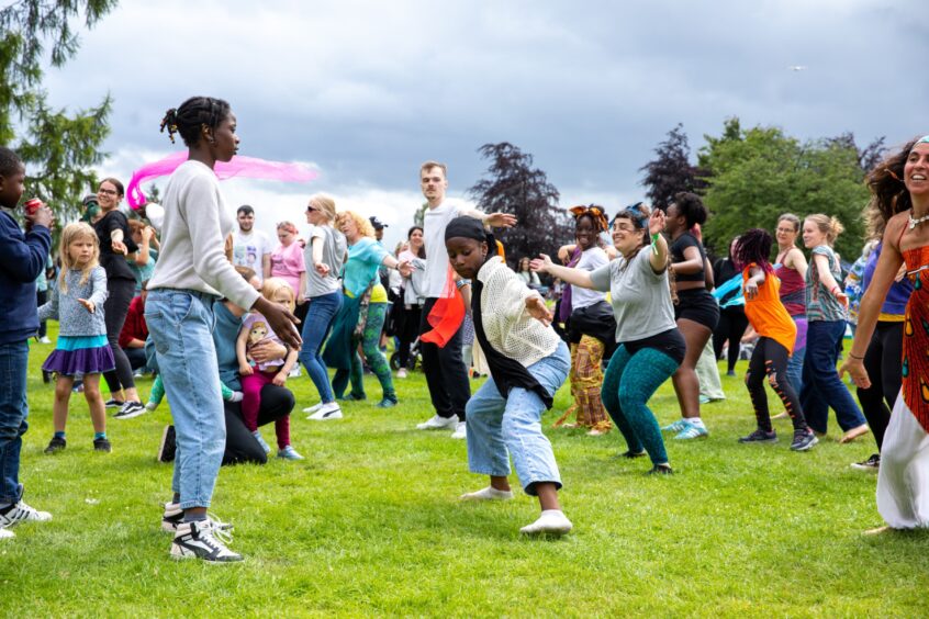 A large, diverse crowd dances energetically on the grass during an Afrobeat-inspired group session at the Afro-Caribbean Summer Festival in Dunfermline.