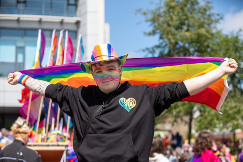 Taylor-Lewis McCleary wearing a rainbow hat and face paint, holding a pride flag behind them at Fife Pride 2025 in Kirkcaldy.